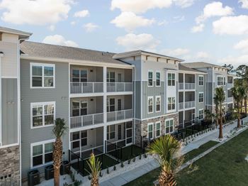 A row of modern apartment buildings with balconies and palm trees in front at The Quinn Luxury Apartments, Pensacola, FL, 32526